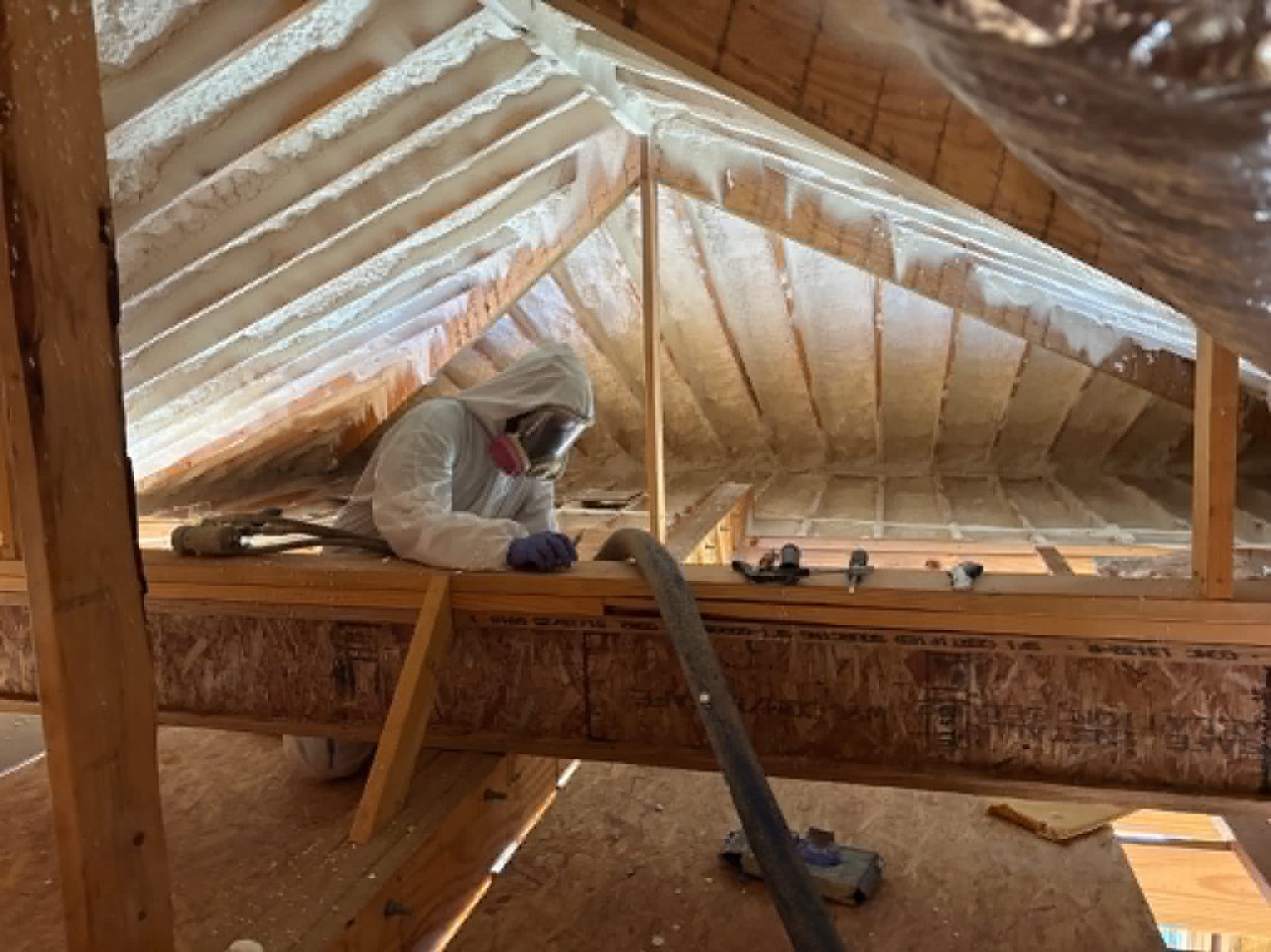 Spray foam worker in full PPE applying foam in attic South Louisiana